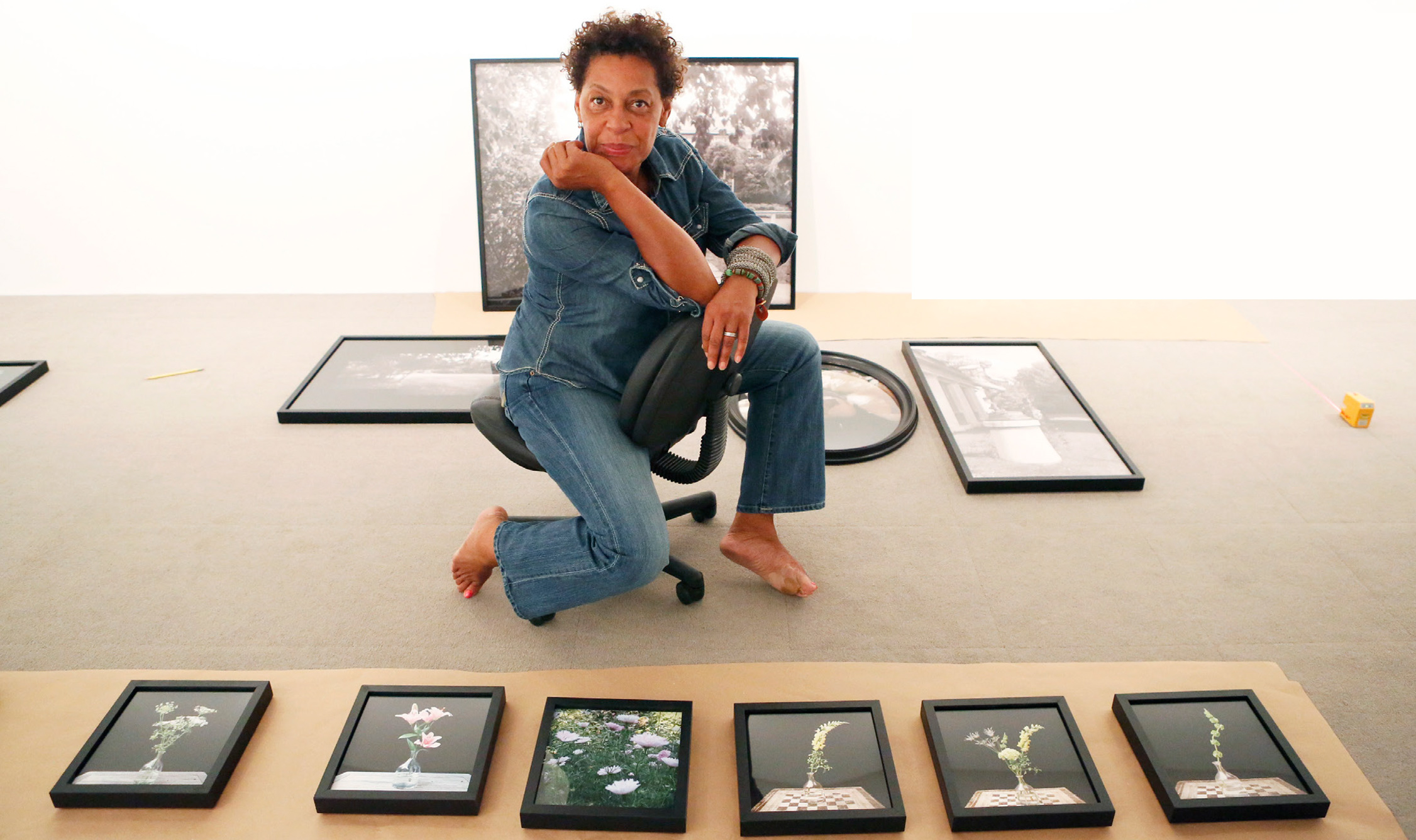 An image of Carrie Mae Weems kneeling in front of her work in black frames. 