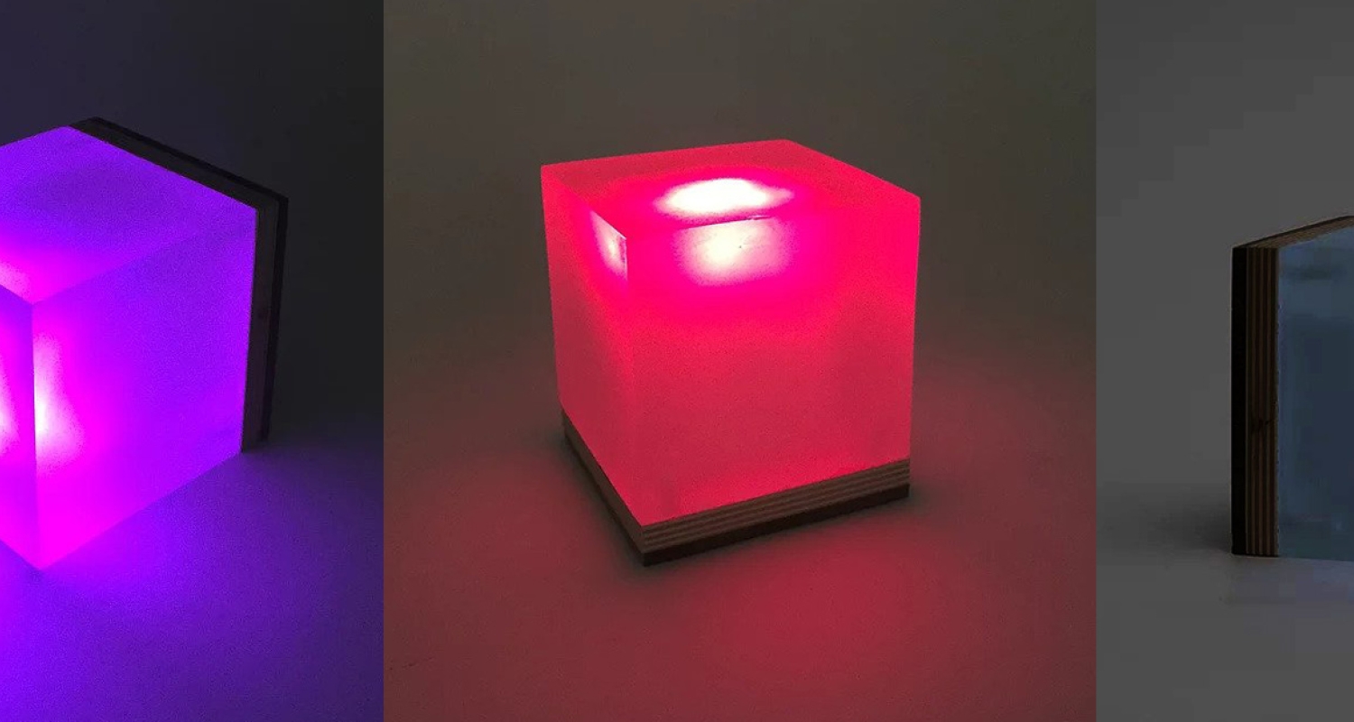 Three different images side-by-side featuring an illuminated cube/lamp-like object. In each image, the cube is a different color and is facing a different direction, from left to right: purple (facing left), red (upright), and teal (facing right). The light within the cube is brightest in the center.