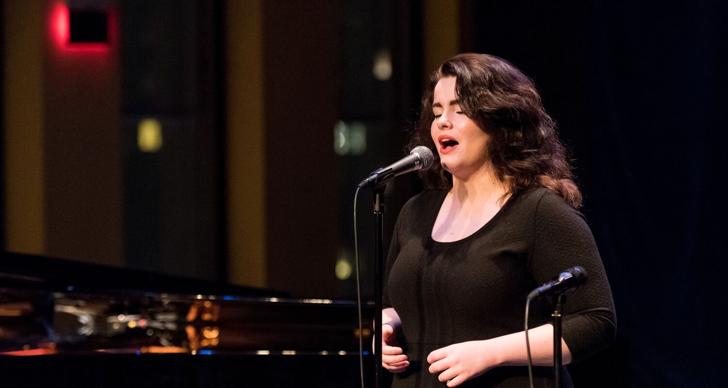 UArts student performs on stage with a mic and piano