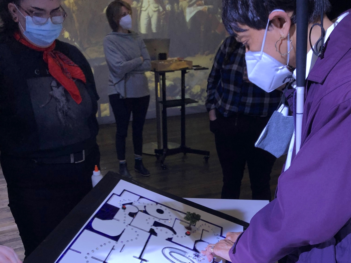 A person in a purple jacket is leaning over a tablet interface, displaying a map of a museum interior with tangible waypoints. 