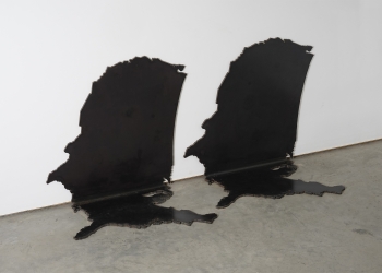 Two black steel sculptures of the map of the US with the northeast part of the country flat on the floor and the rest of the country sitting vertically against the wall