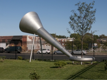 A large silver outdoor funnel made of steel that provides extra water to the tree the sculpture encircles 