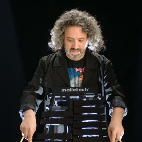 Tony Miceli wearing black in front of a black background and holding a black vibraphone and wooden mallets