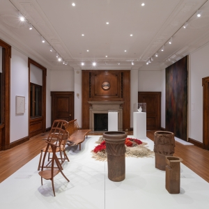 Invisible City Exhibition, Gallery B: raised platform in foreground displaying clay pots and wooden furniture with grand fireplace in background
