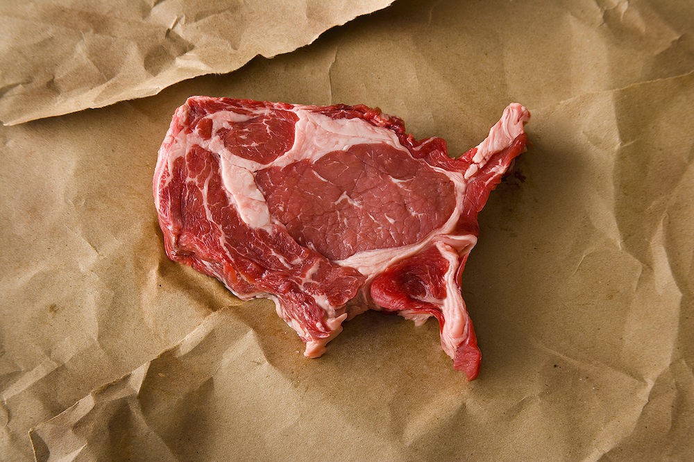 A piece of steak cut into the shape of the U.S. on brown paper