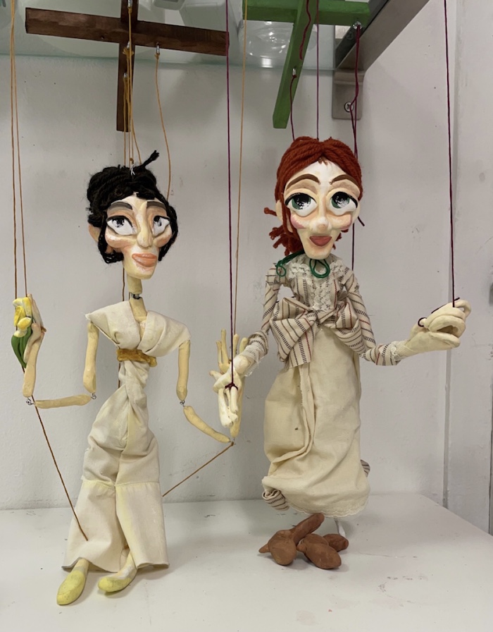 Two puppets of women in the 1800s made from found and recycled materials.