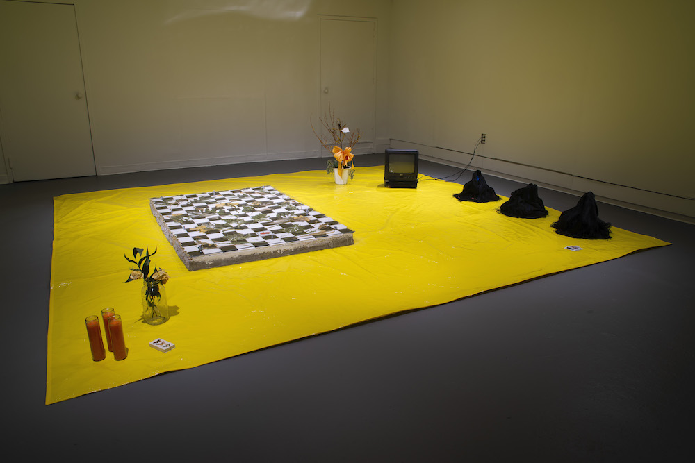 A chess board, TV, flowers and candles sit on a yellow sheet