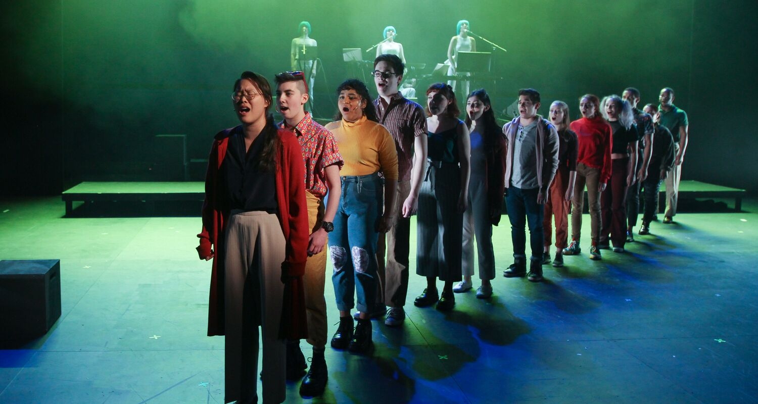 theater students singing on stage in a straight line under green lighting
