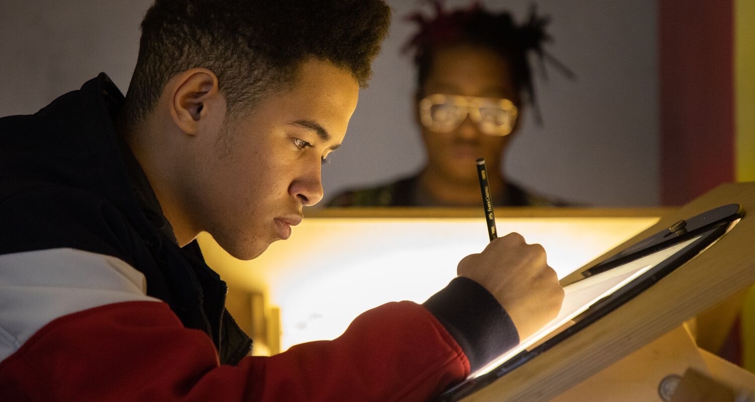 A student, holding a pencil, works in an Animation class. 