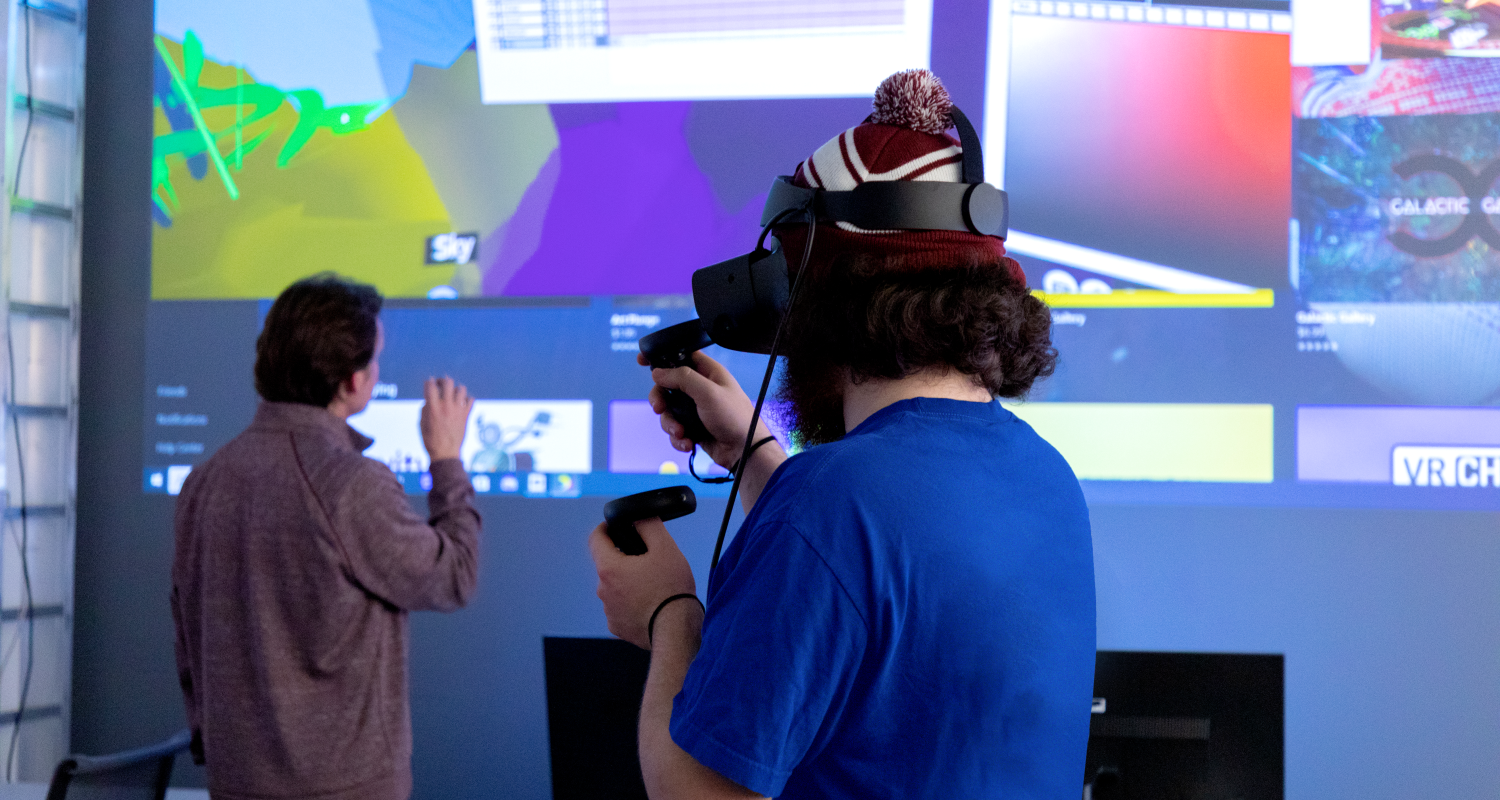 UArts student and professor demo a VR headset against an electronic screen with graphics on it