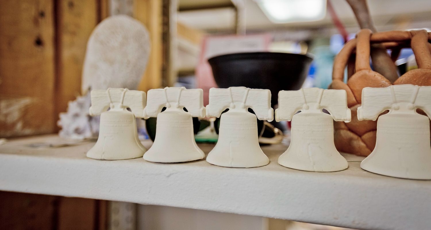 A row of five unfinished ceramic Liberty Bells on a workshop table. 