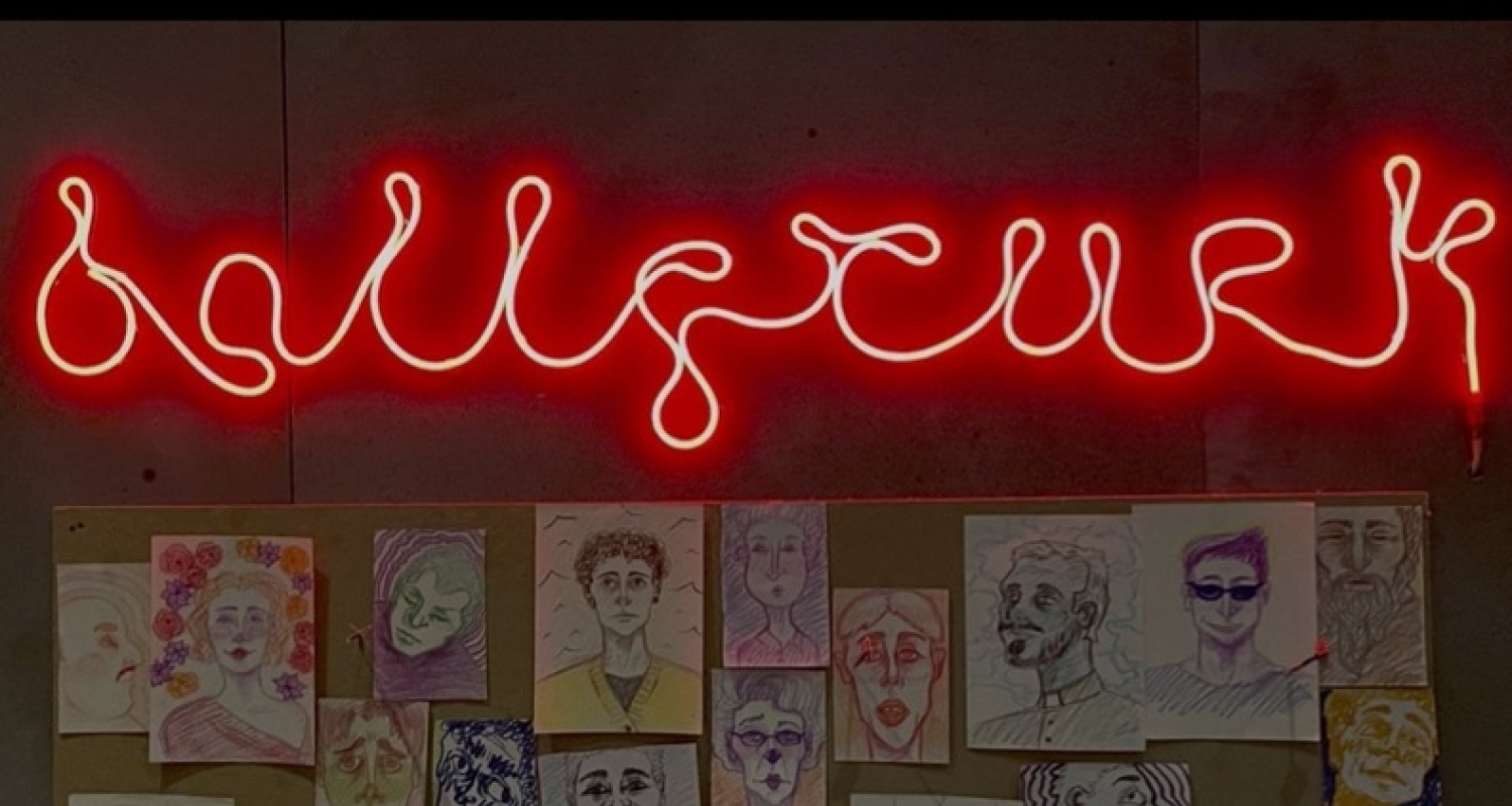 A grey wall with a tan cork board, full of multi-color images of different faces, drawn using pen, marker, and crayons. Above the faces is a red glowing sign that reads "Ballyturk". At the bottom of the image the line reads "Caplan Studio Theater OCT. 28, 30 2021 7:30 P.M., OCT. 31 2021 2 P.M." followed by "For tickets and showtimes, visit tickets.uarts.edu, or call 215-717-6310".