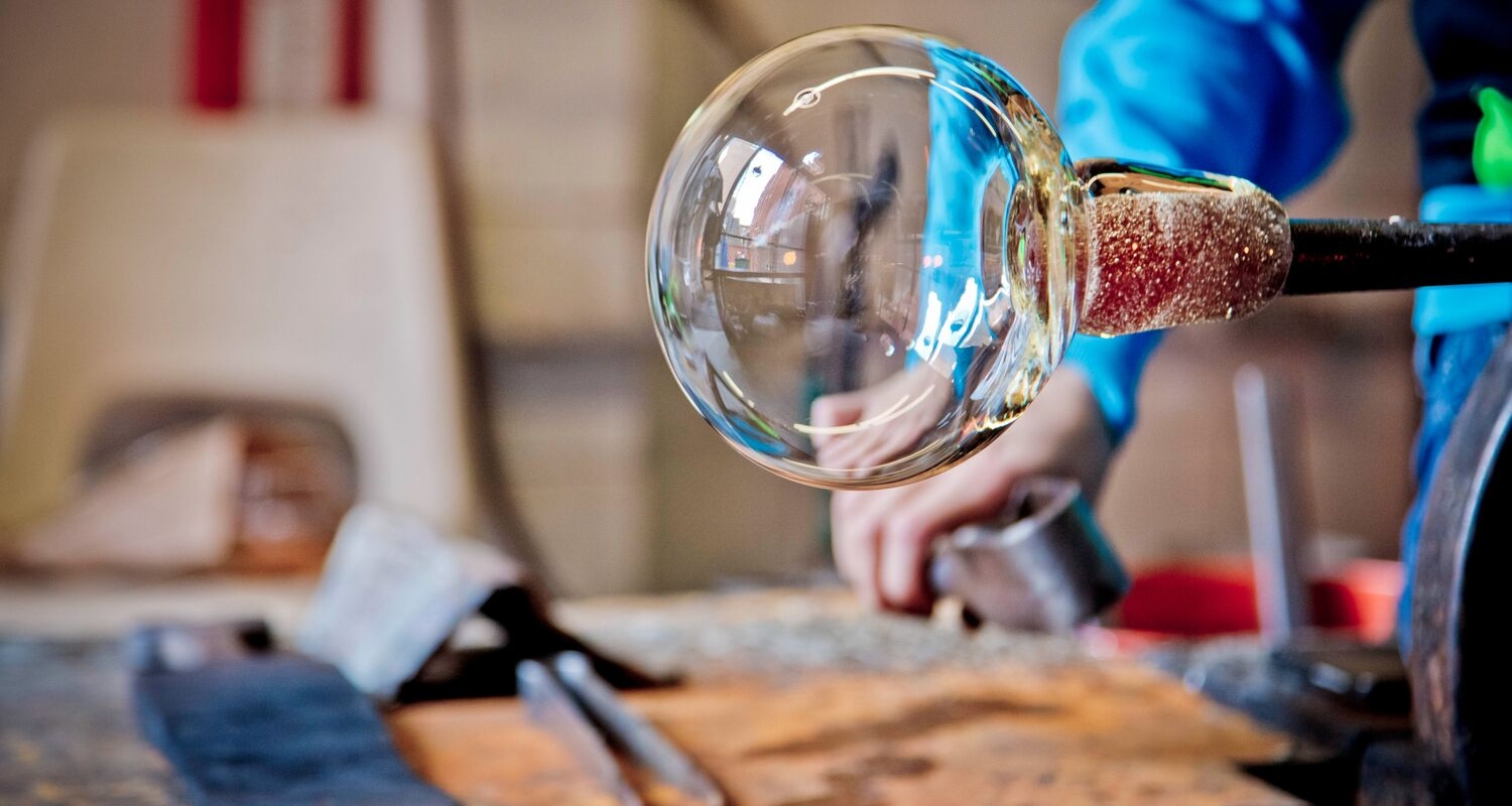 A glass orb, in process, being held over a worktable. 