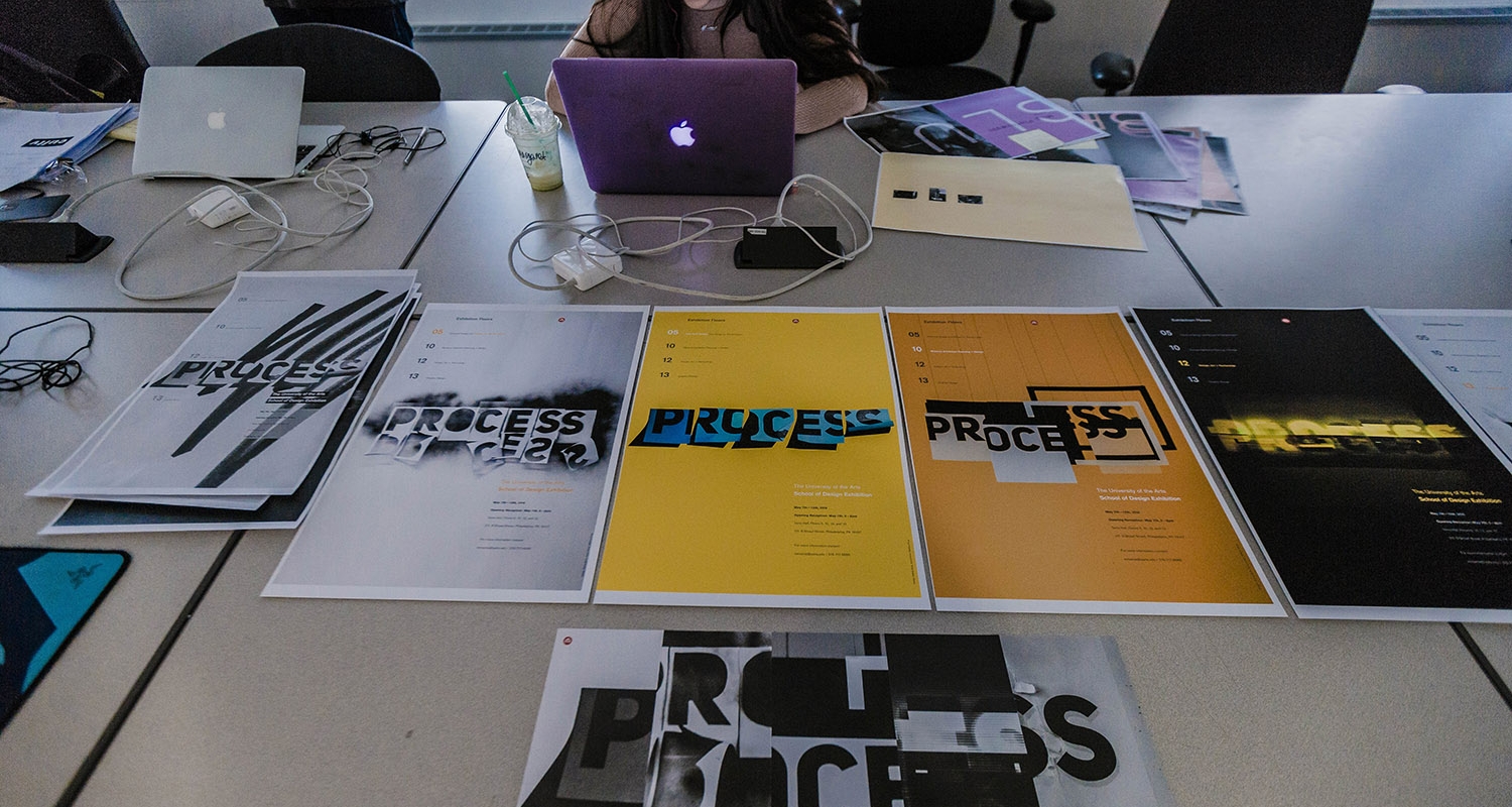 A student sits at a large worktable with the word "Process" in different graphic treatments.