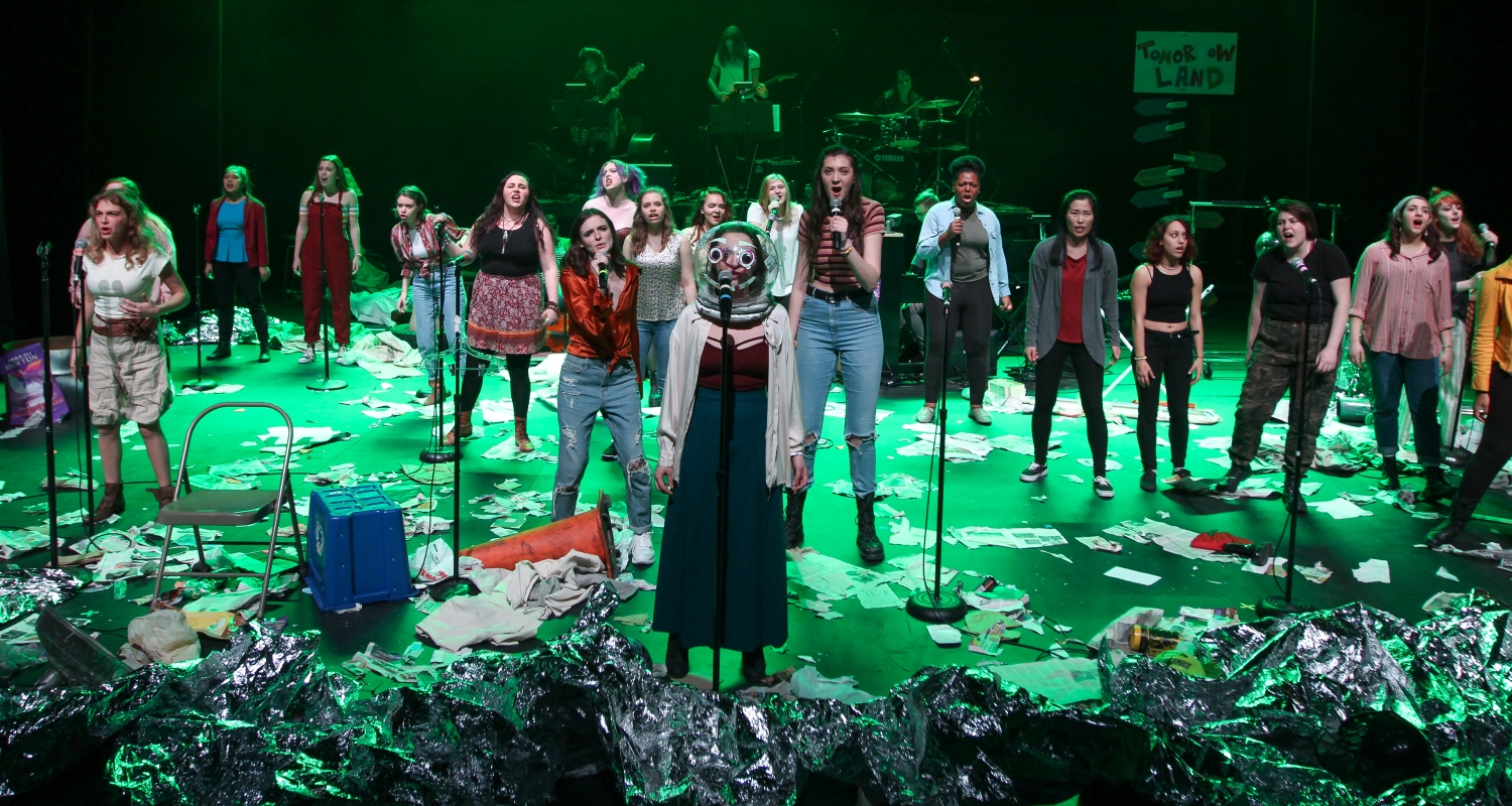 A group of actors perform on a littered stage. 