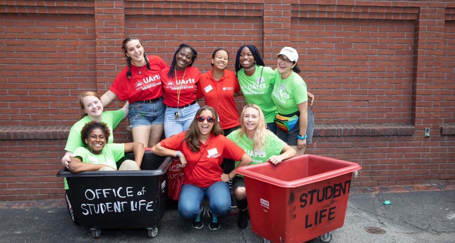 Nine Resident Assistants in a group photo smiling wearing red and green UArts shirts.