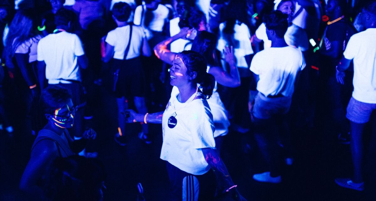 Students dancing wearing white shirts in a black light.