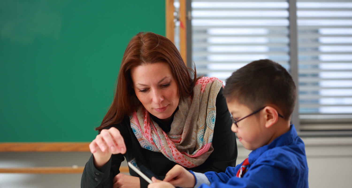 A woman teacher with a young male student, holding a tablet. 