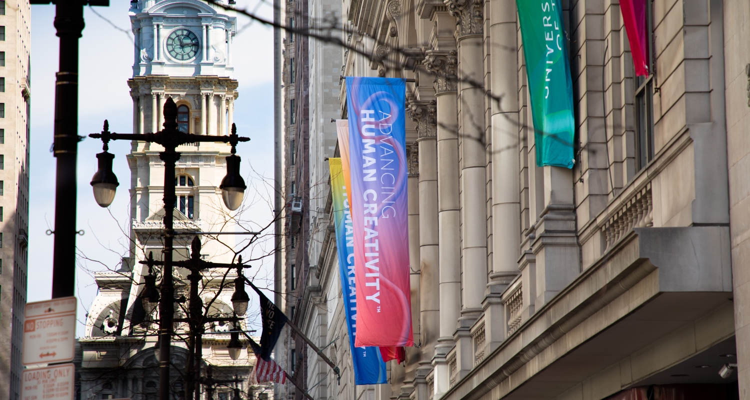 Colorful banners adorn the facade of the Terra Hall building. The iconic City Hall building is visible in the background. "Advancing Human Creativity" is featured on the banners.