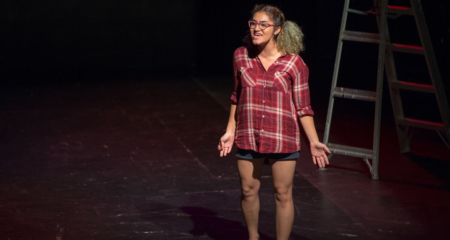 A student acts out their monologue on stage in front of a ladder