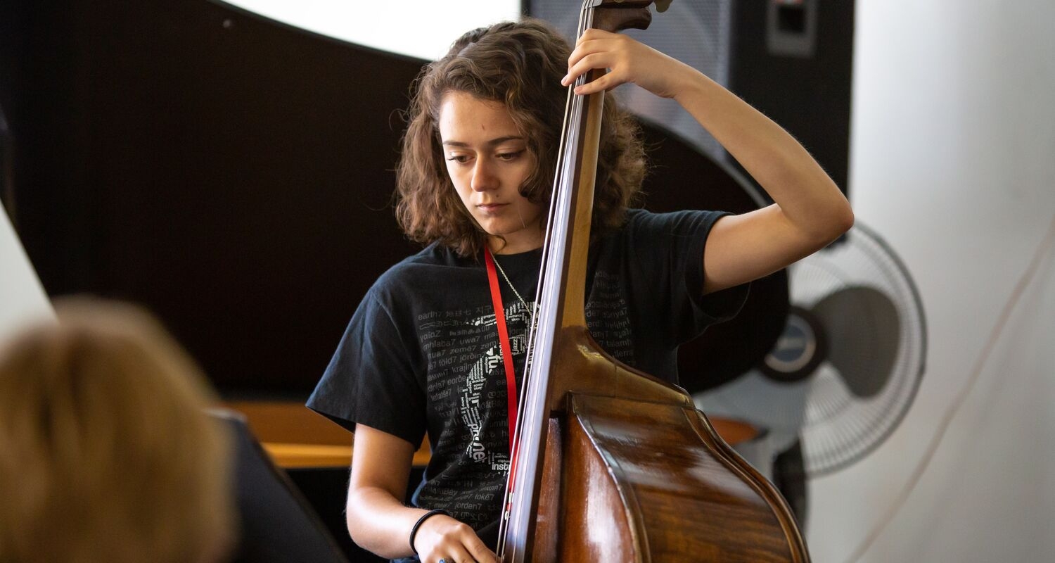 An upright bass student musician standing in front of a piano and focusing on sheet music