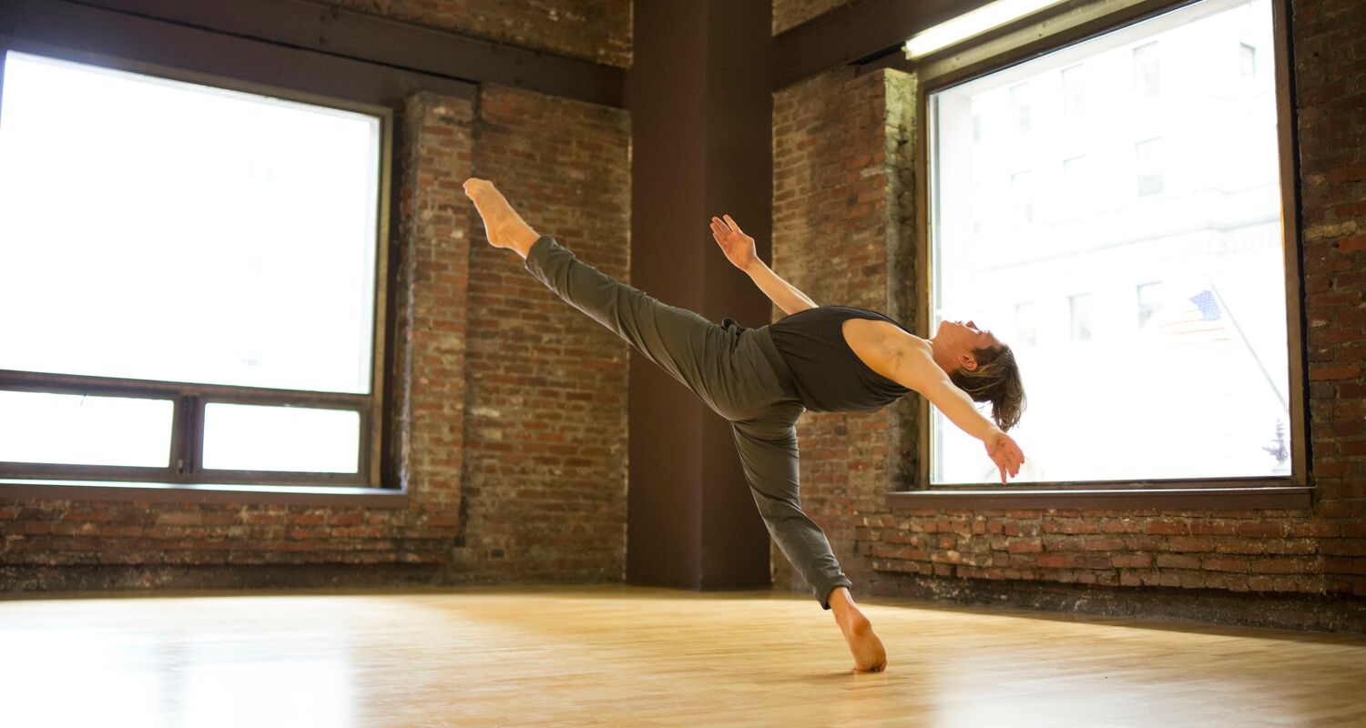 A dancer extends their leg into the air in a dance studio.