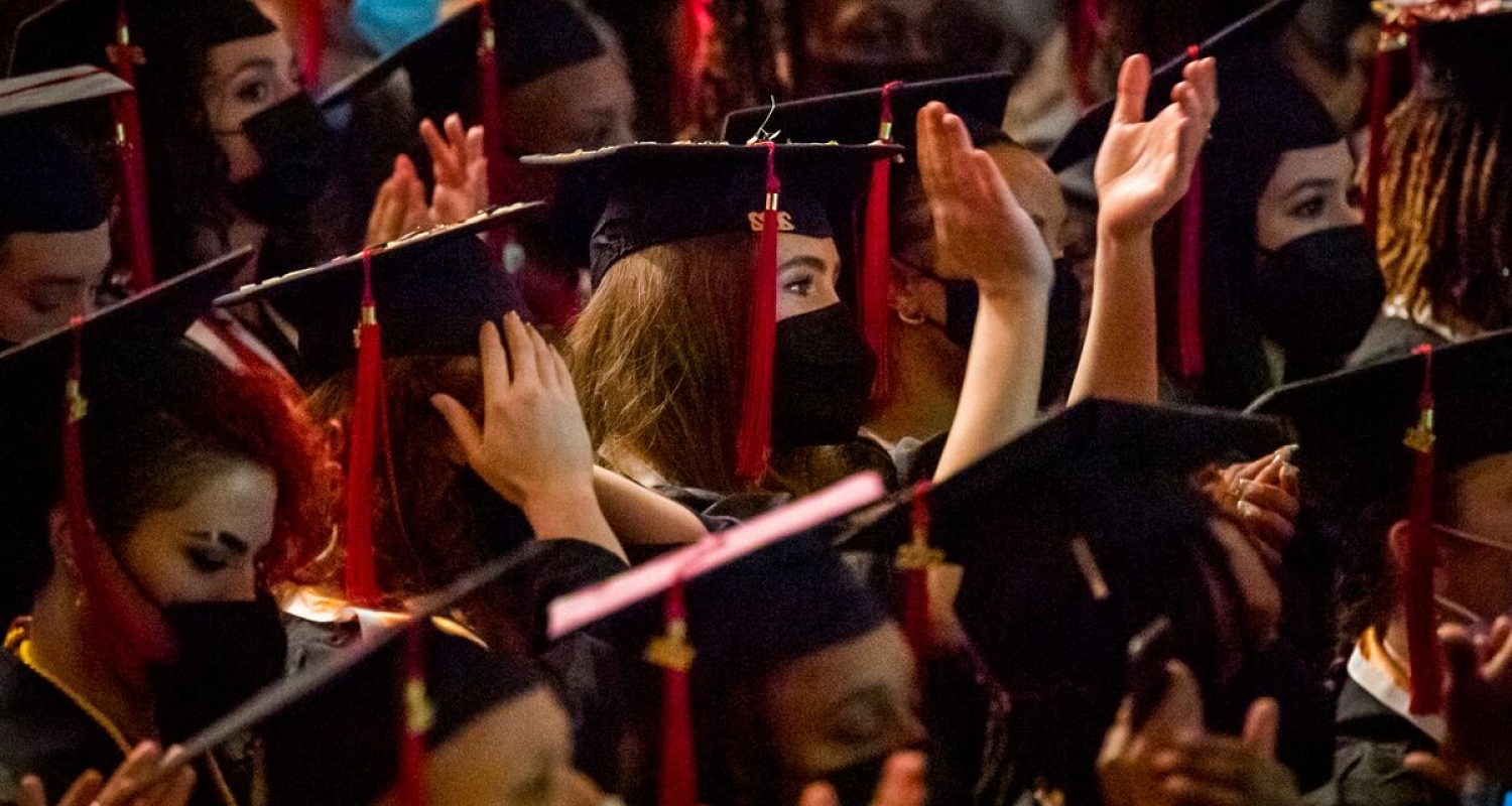 students in graduation regalia applaud during commencement 2022