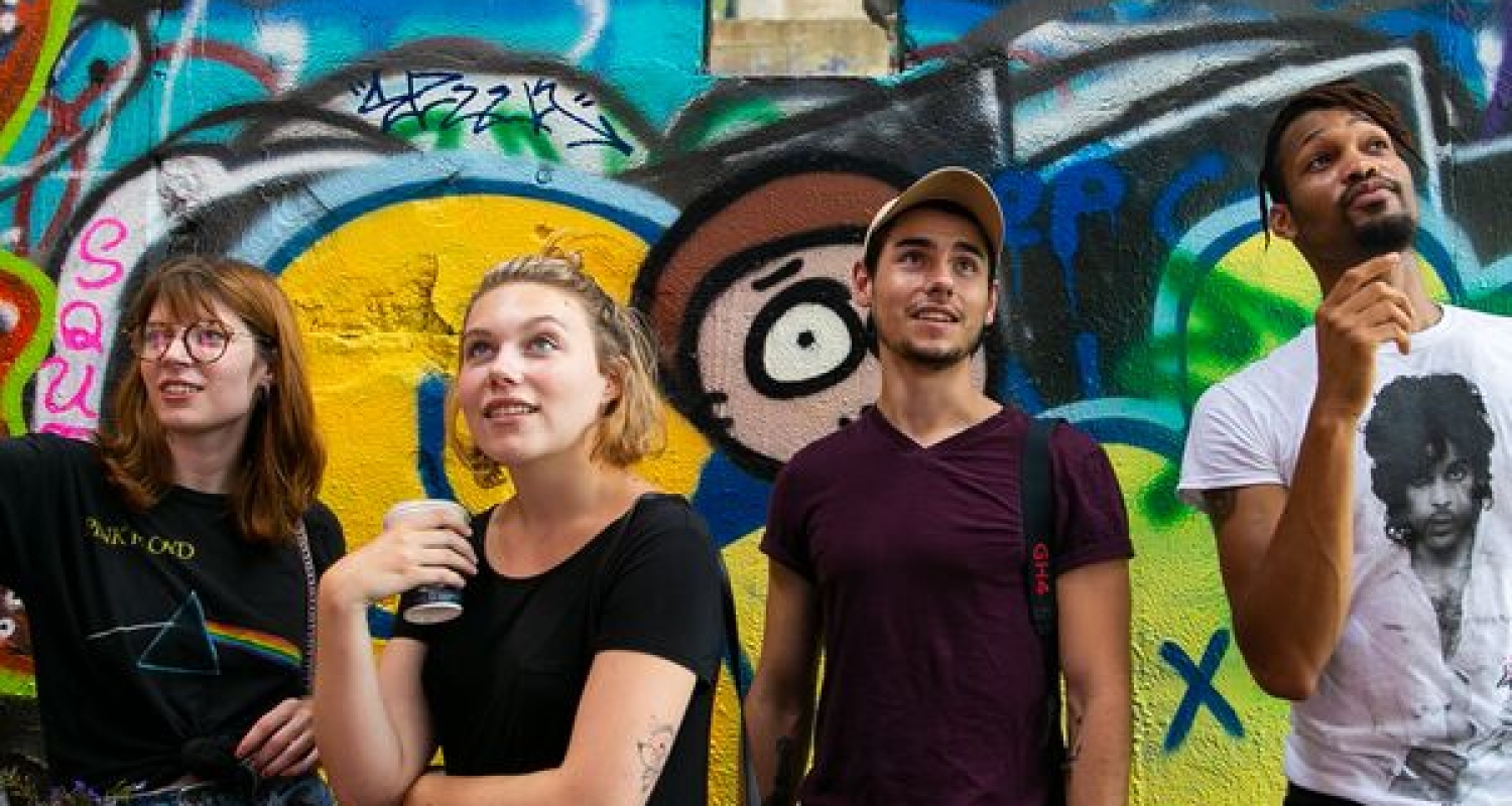 Four students standing in front of a wall of graffiti.