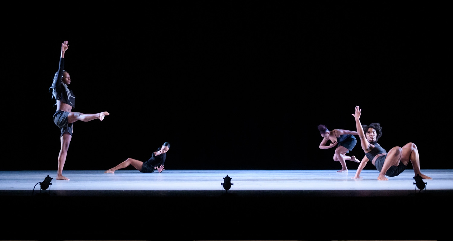Dance students perform on a stage under a white spotlight