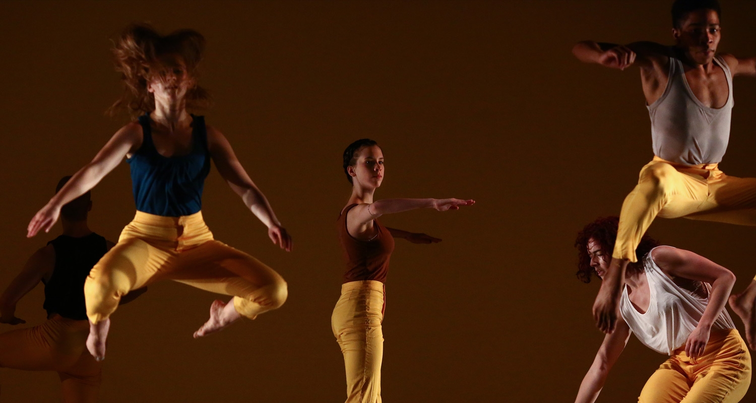 Dance students perform on a stage in yellow costumes