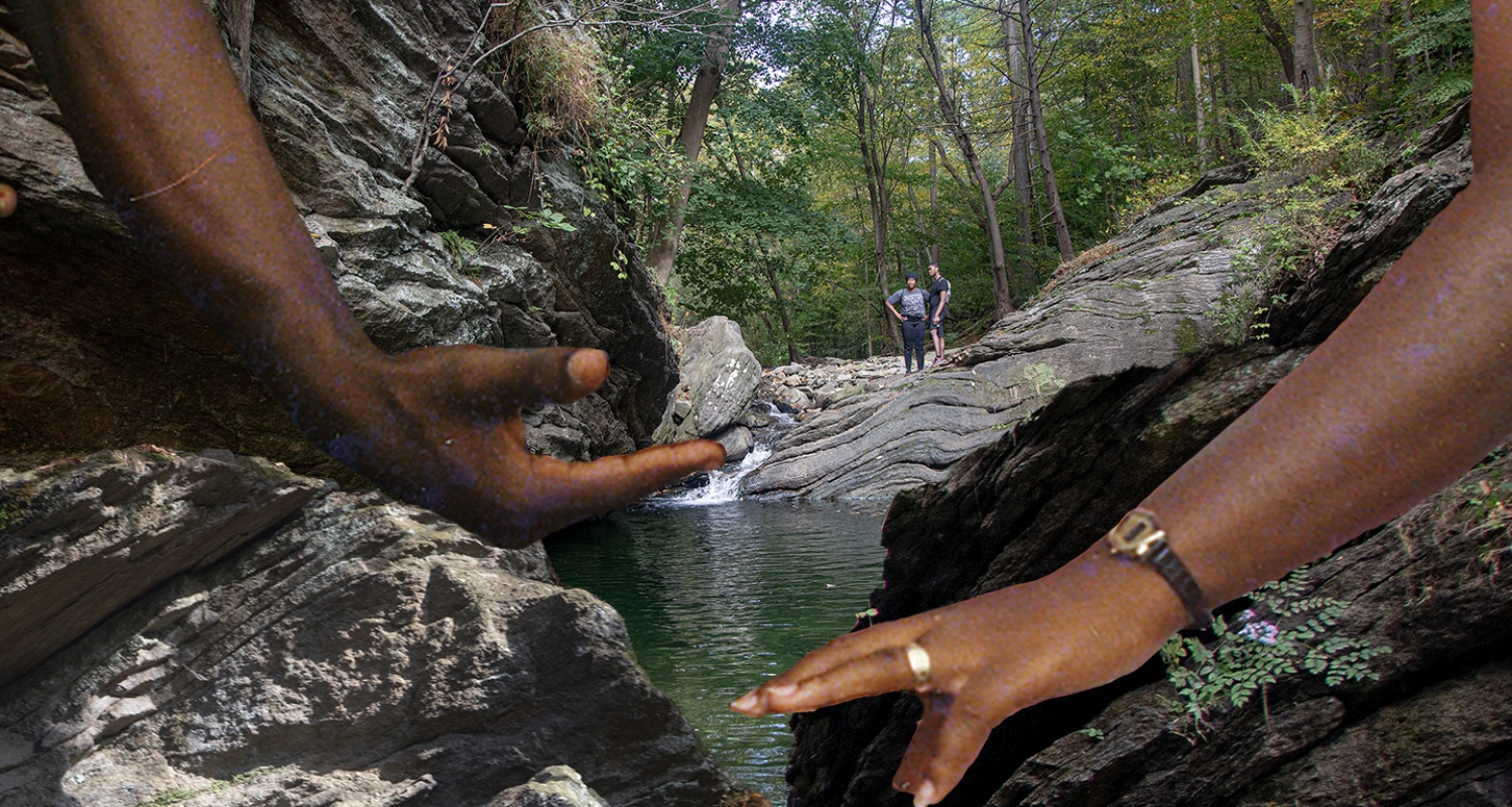 Two Black hands reaching towards one another against a landscape with trees, rocks and water