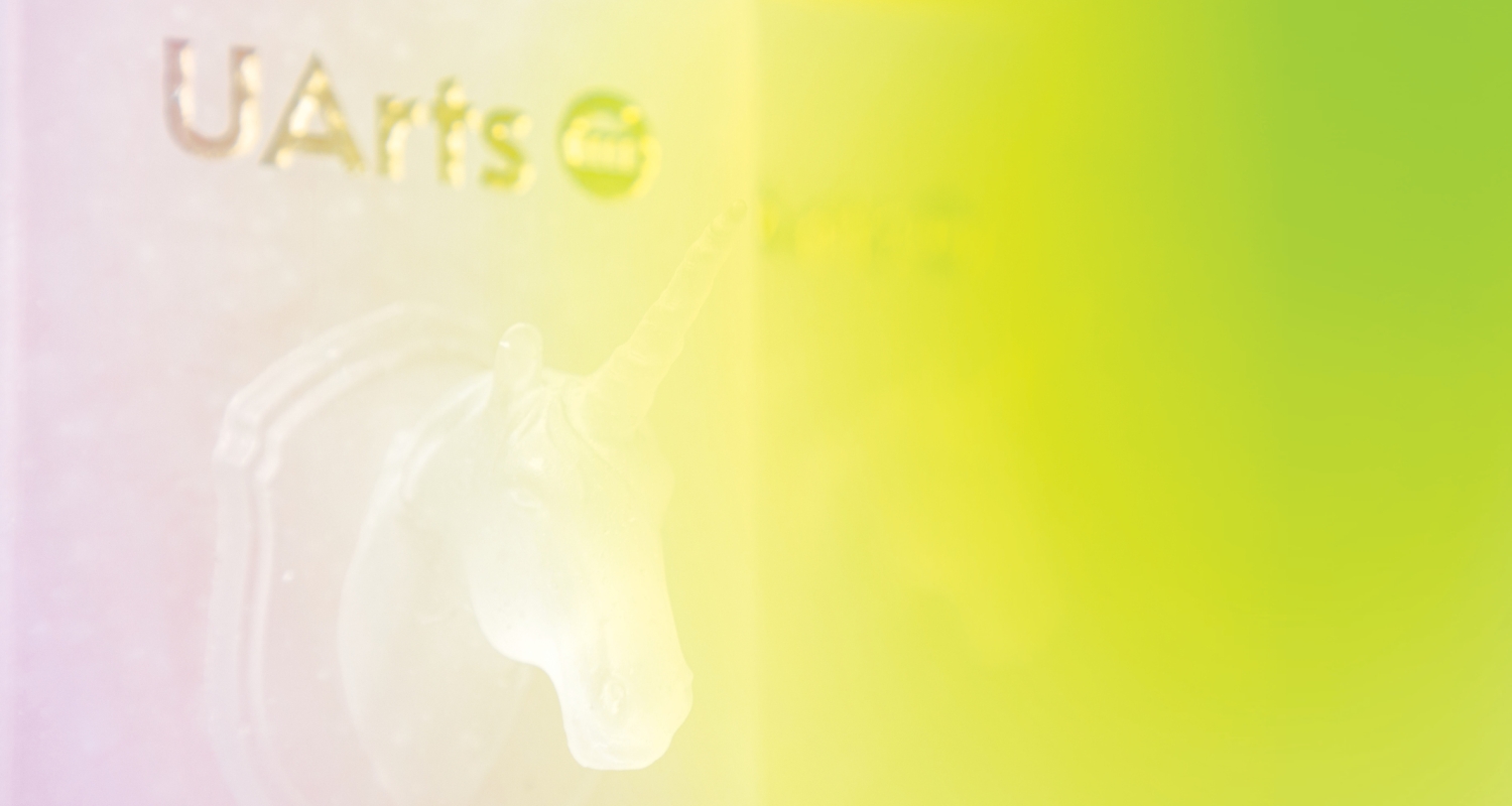 a slightly pink-peach to lime green gradient is overlaid left to right across a zoomed in image of a trophy sitting on the left. it consists of a frosted glass unicorn and uarts written in gold