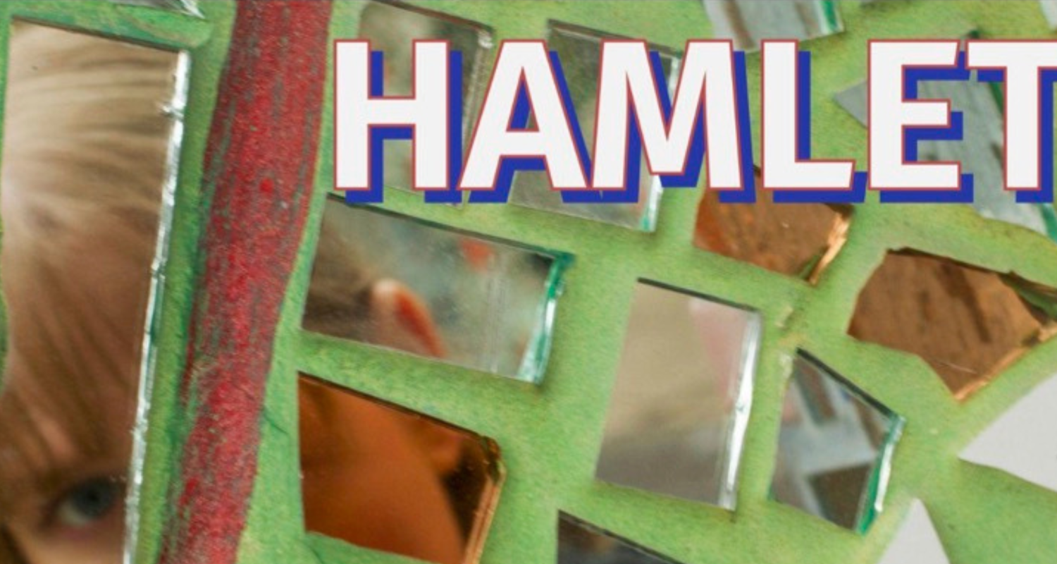 A bright green wall with mirror pieces attached. In the mirror a person’s face is seen. The writing reads “Hamlet”. 