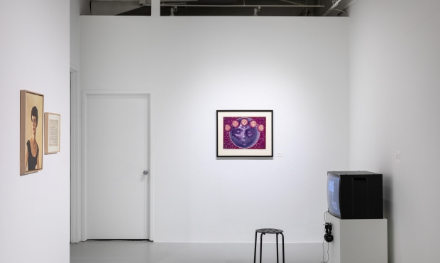 Photo of gallery installation of Dream Dance with two pieces of artwork in the backgroun--a purple face facing the viewer and a portrait on a side wall––with a television and stool in the foreground