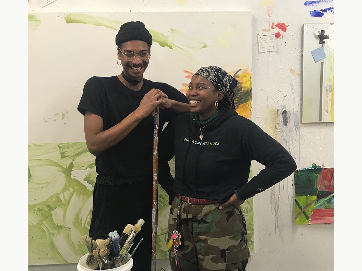 Two students stand and laugh together in the painting studio