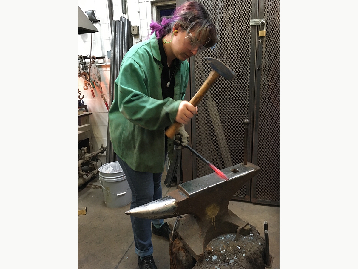 A student hammers fired metal on an anvil