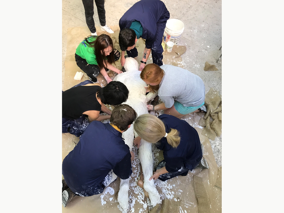 Sculpture students and faculty work on molding a human body