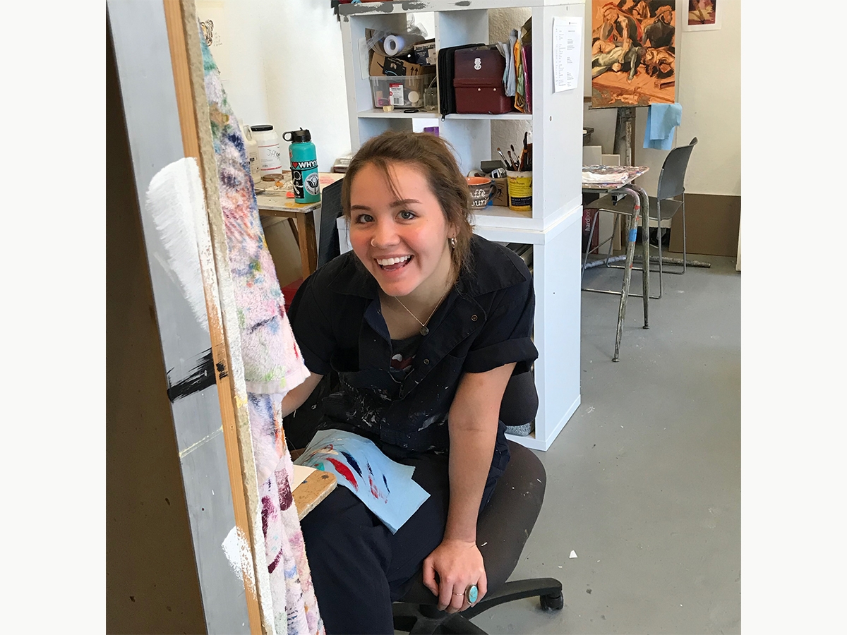 A student smiles at the camera while working on their art in the painting studios.