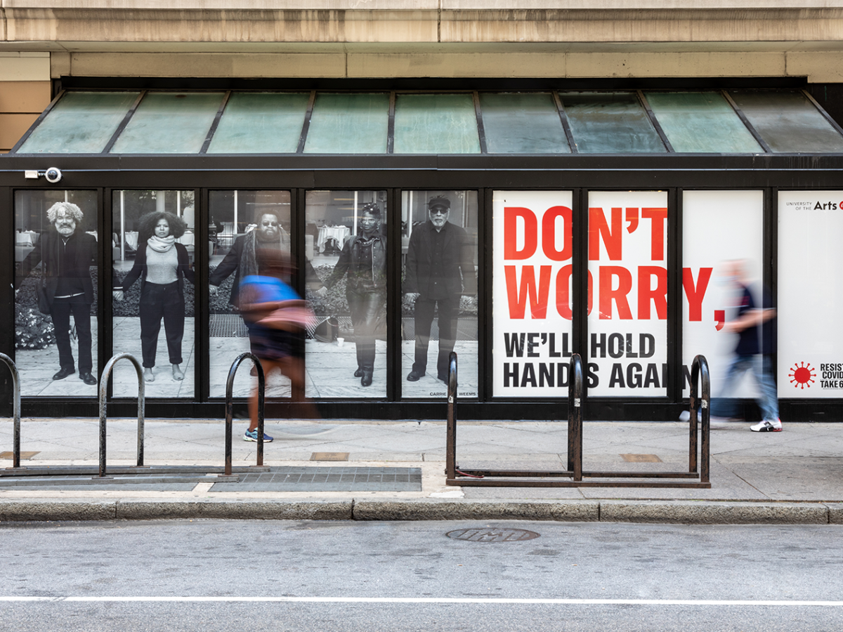 An image of a billboard with people holding hands that says "don't worry, we'll hold hands again" in red typeface.