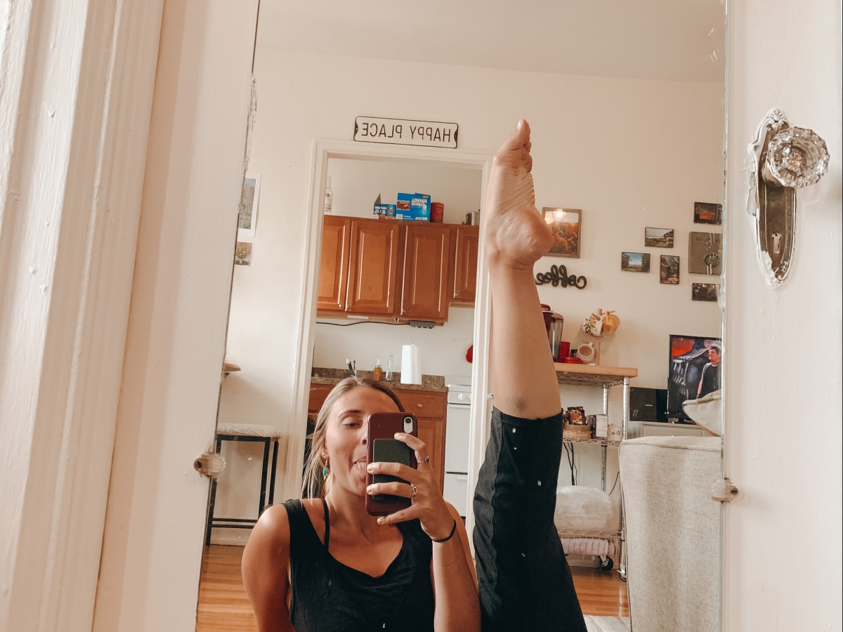 Selfie of Emily through their mirror with leg extended in the air in a dance pose