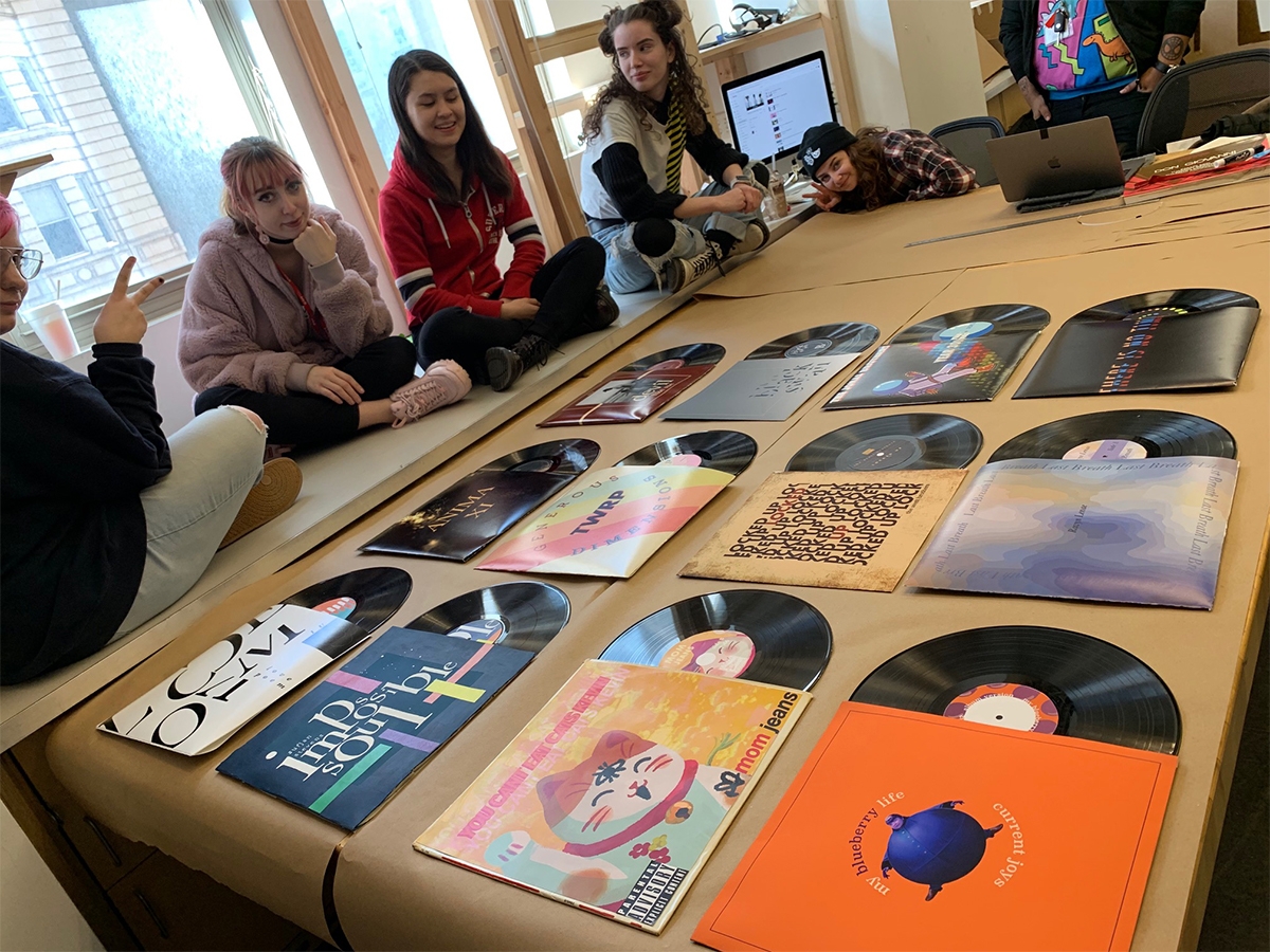 Students sit around a set of album covers that they designed. 