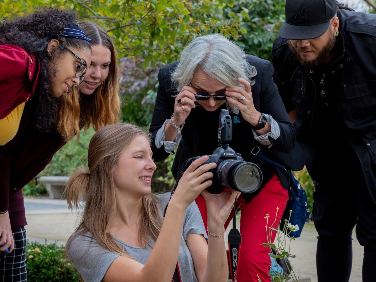 Students and faculty gather around their DSLR to review photos during an outdoor shoot.