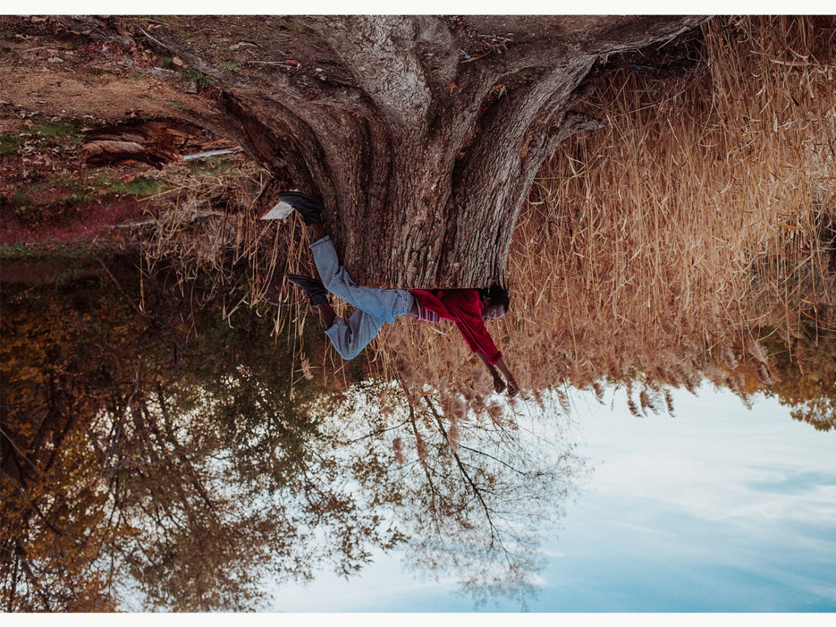 An upside-down photograph of a figure laying on a tree stump in front of a field of hay