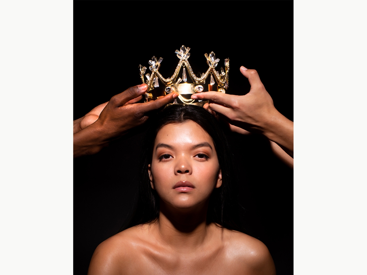 A photo of a two hands placing a gold crown on the head of a woman