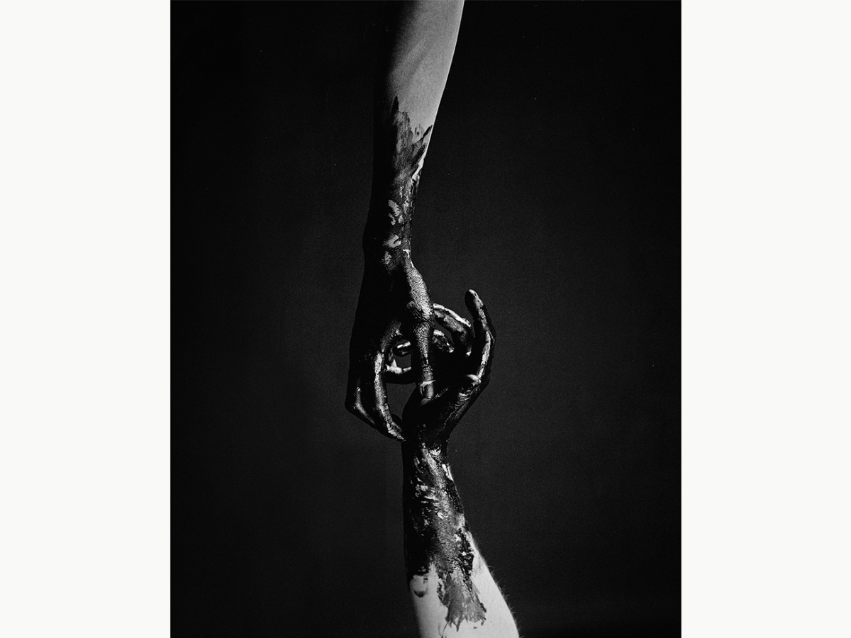 A photography of two hands reaching out to each other covered in black paint
