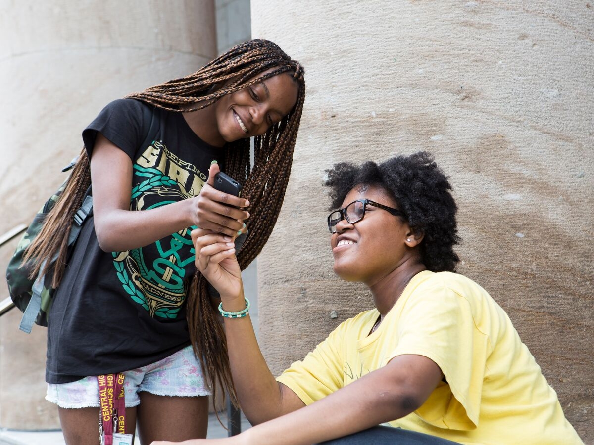 Students sit on the steps of Hamilton and share images on their phone