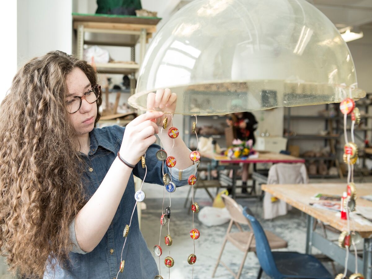 A Sculpture student hangs bottle caps from a dome