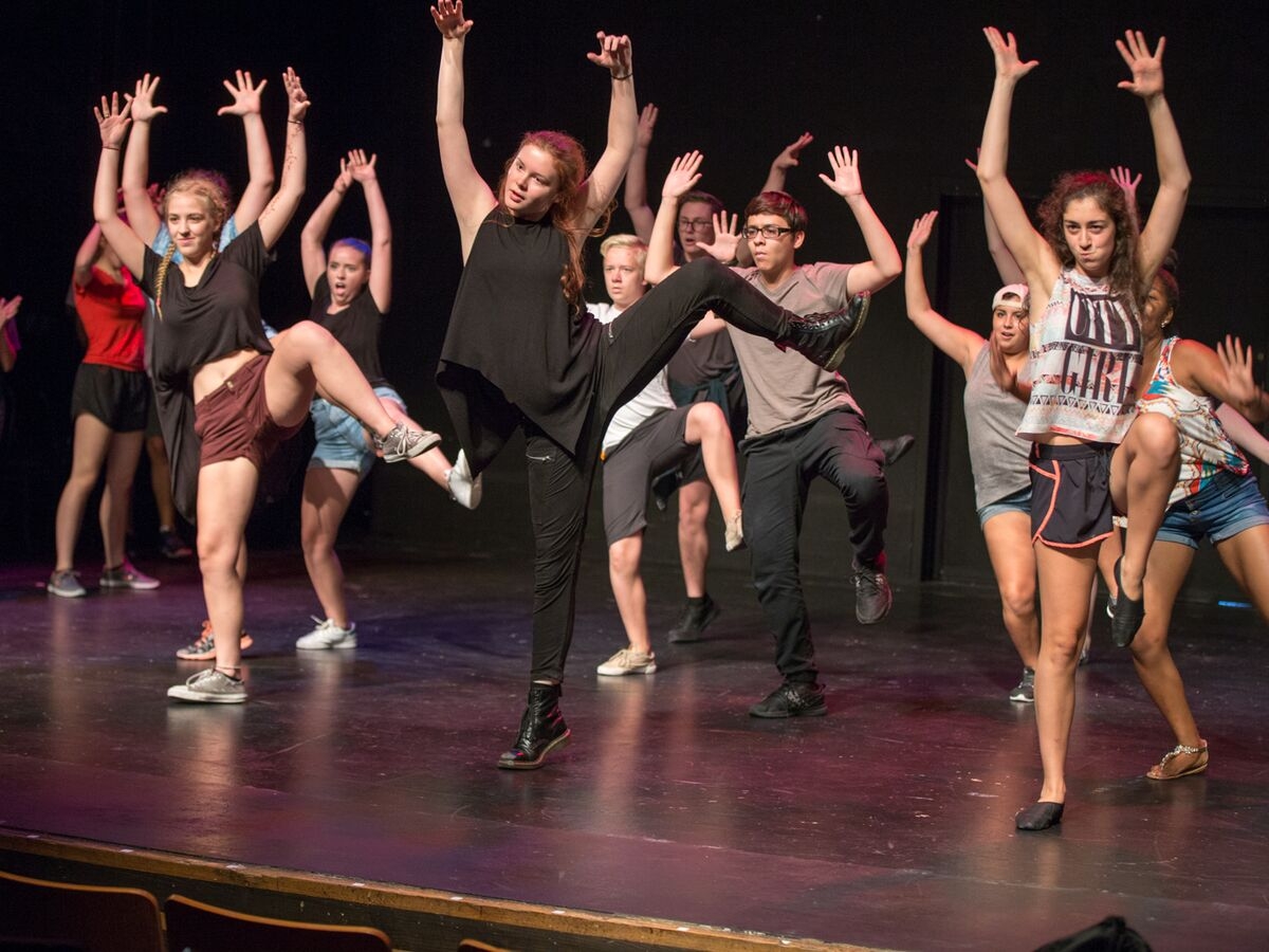 Theater students throw their hands and leg into the air on stage
