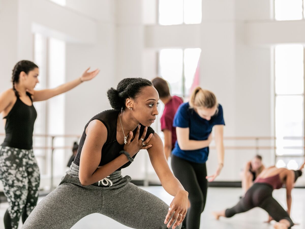 A dancer touches their shoulder while getting low to the ground during dance class