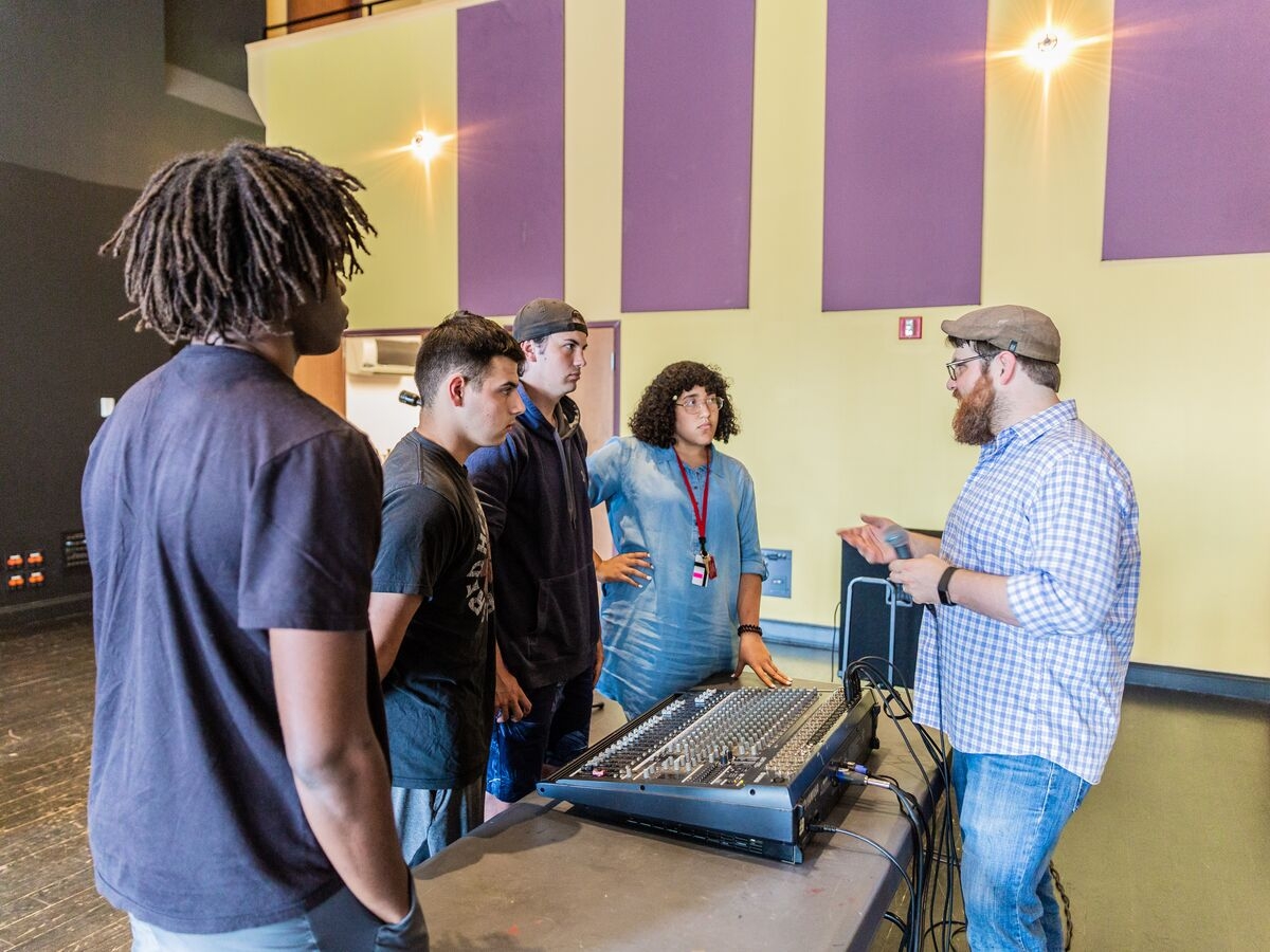 Students discuss audio production around a mixing board